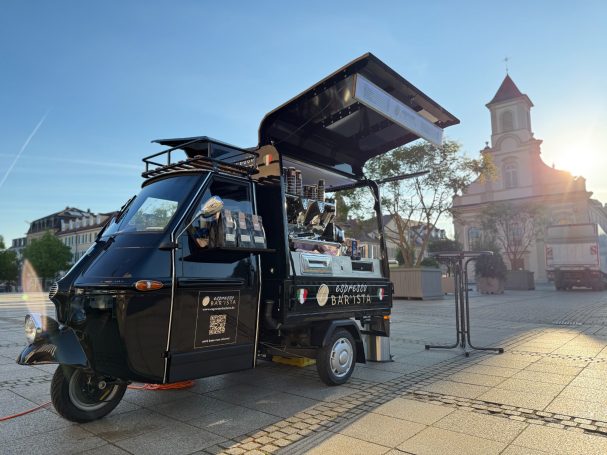 Ein schwarzer Foodtruck mit geöffnetem Dach, im Hintergrund ein Kirchturm.