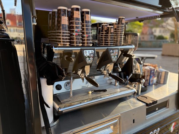 Kaffeewagen mit Espressomaschine und Kaffeetassen im Hintergrund.